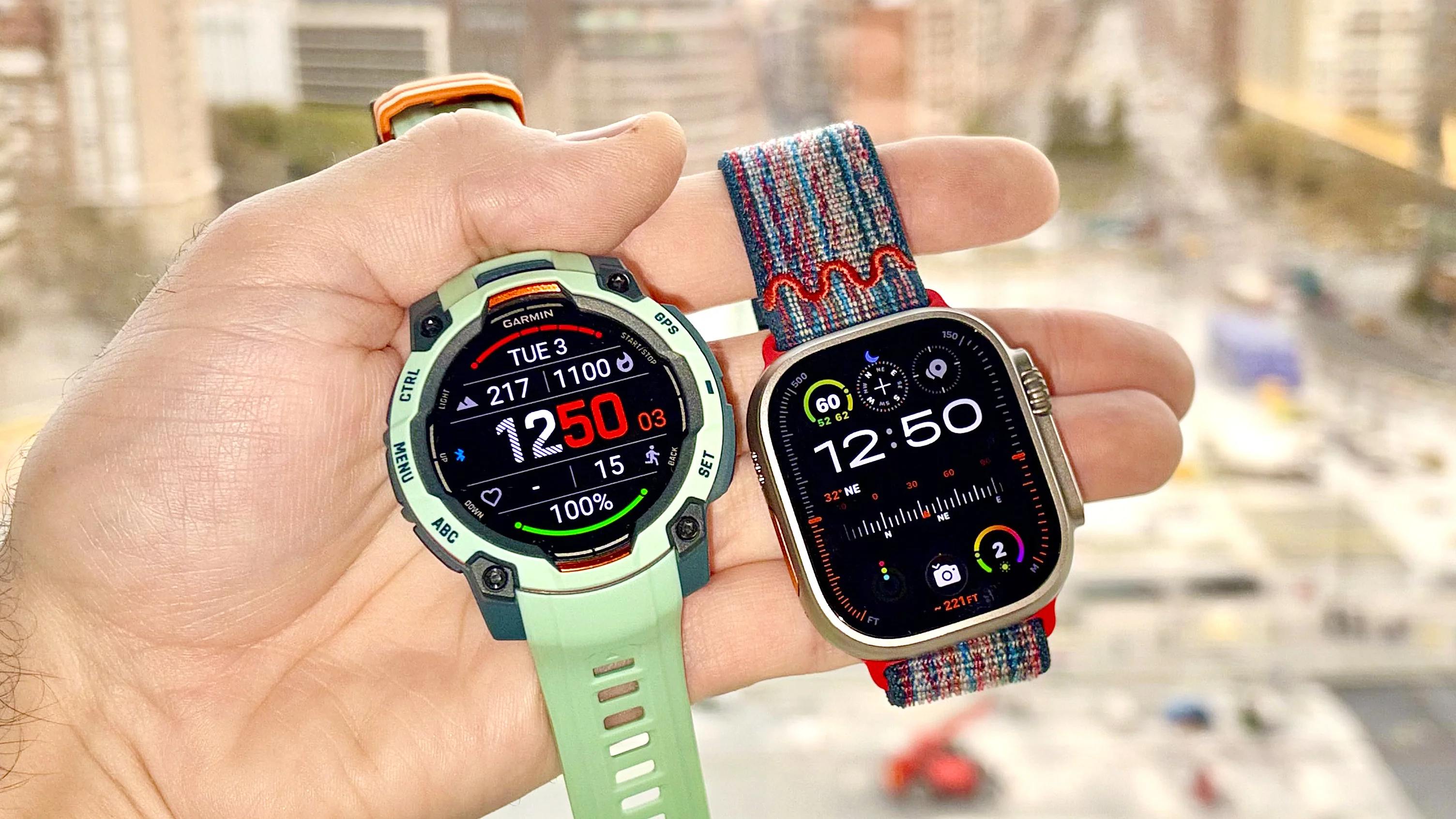 Close-up of the Garmin Instinct 3 next to the Apple Watch Ultra 3 with the Barcelona skyline in the distance